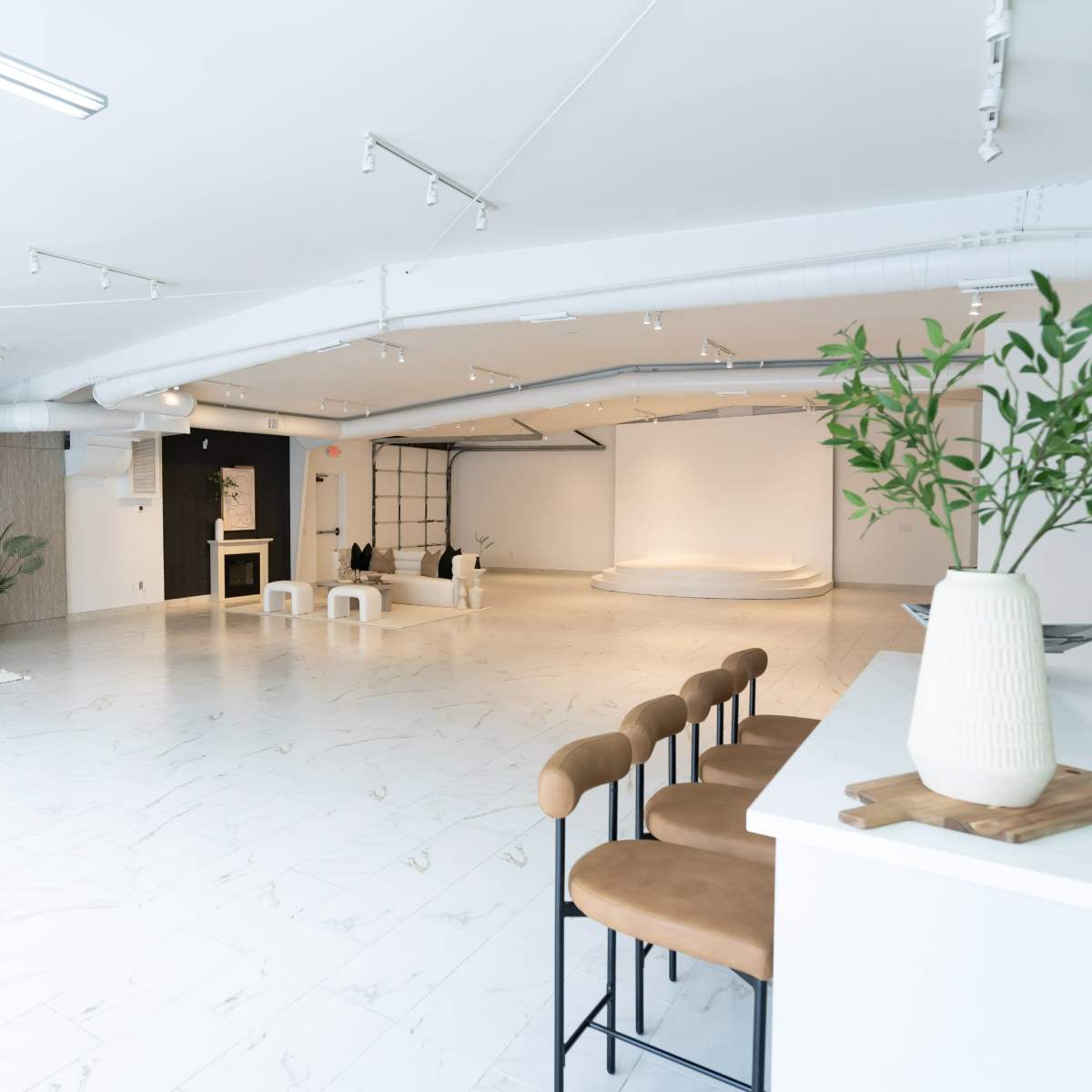 A spacious, modern studio with light-colored flooring, a minimalist design, and a blank backdrop at one end.