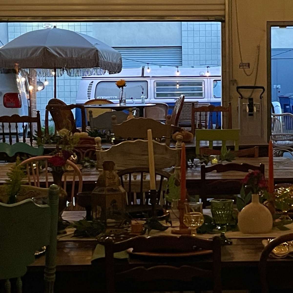 A collection of tables set with various decorations and tableware, with a vintage van visible through an open doorway in the background.