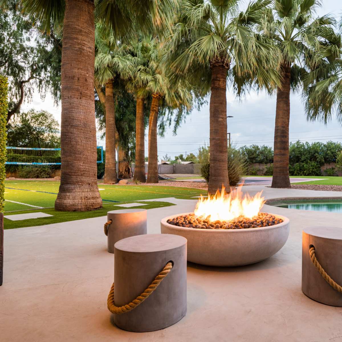An outdoor seating area features a stone fire pit surrounded by palm trees and a swimming pool.