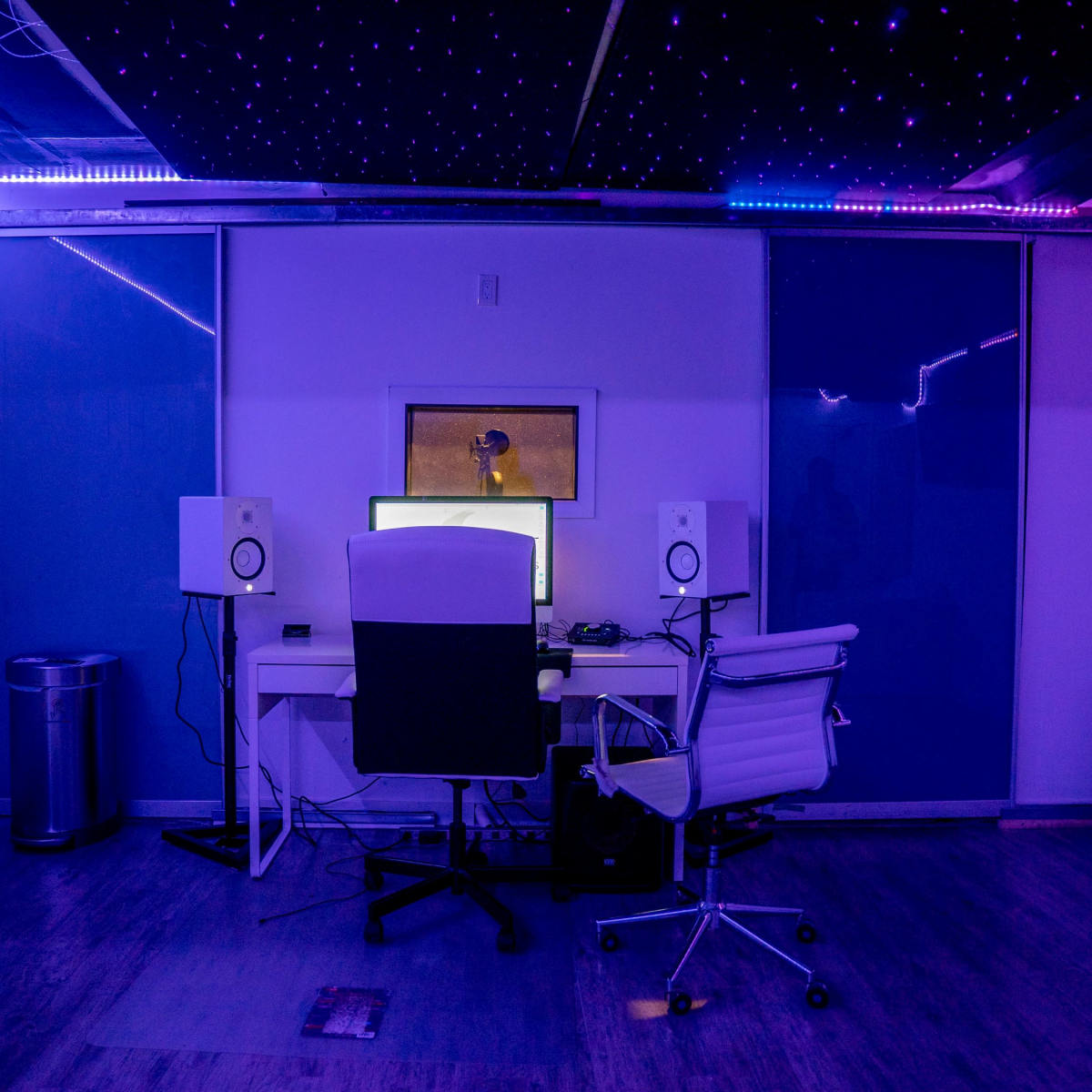 A modern recording studio with a desk, two speakers, and ambient lighting.