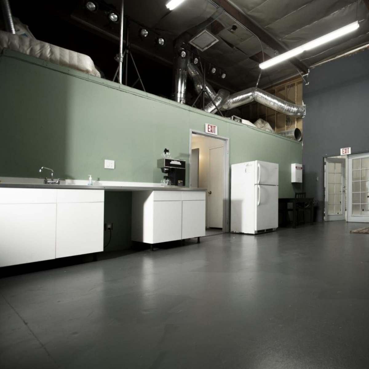 An empty room with a kitchenette on one side, a refrigerator, and a folding table against the wall.