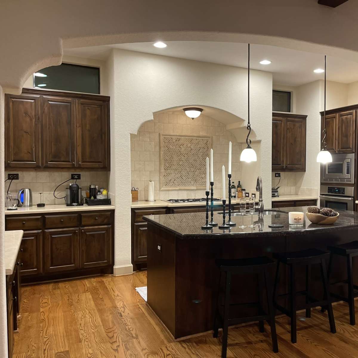 A modern kitchen featuring dark wooden cabinets, a large central island with seating, stainless steel appliances, and a well-lit area with decorative candles.