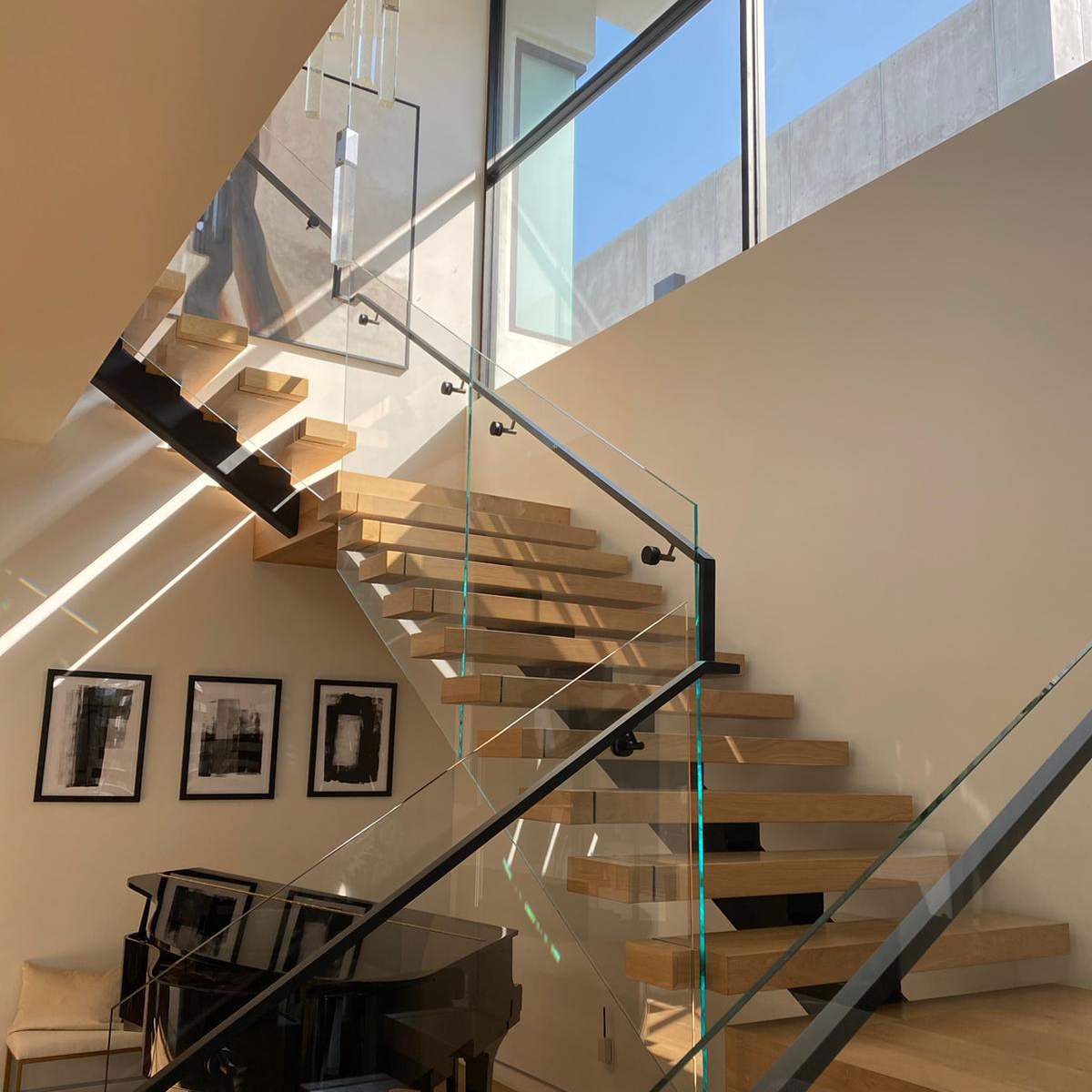 A modern staircase with wooden steps and glass railings, leading up to a large window in a bright interior space.