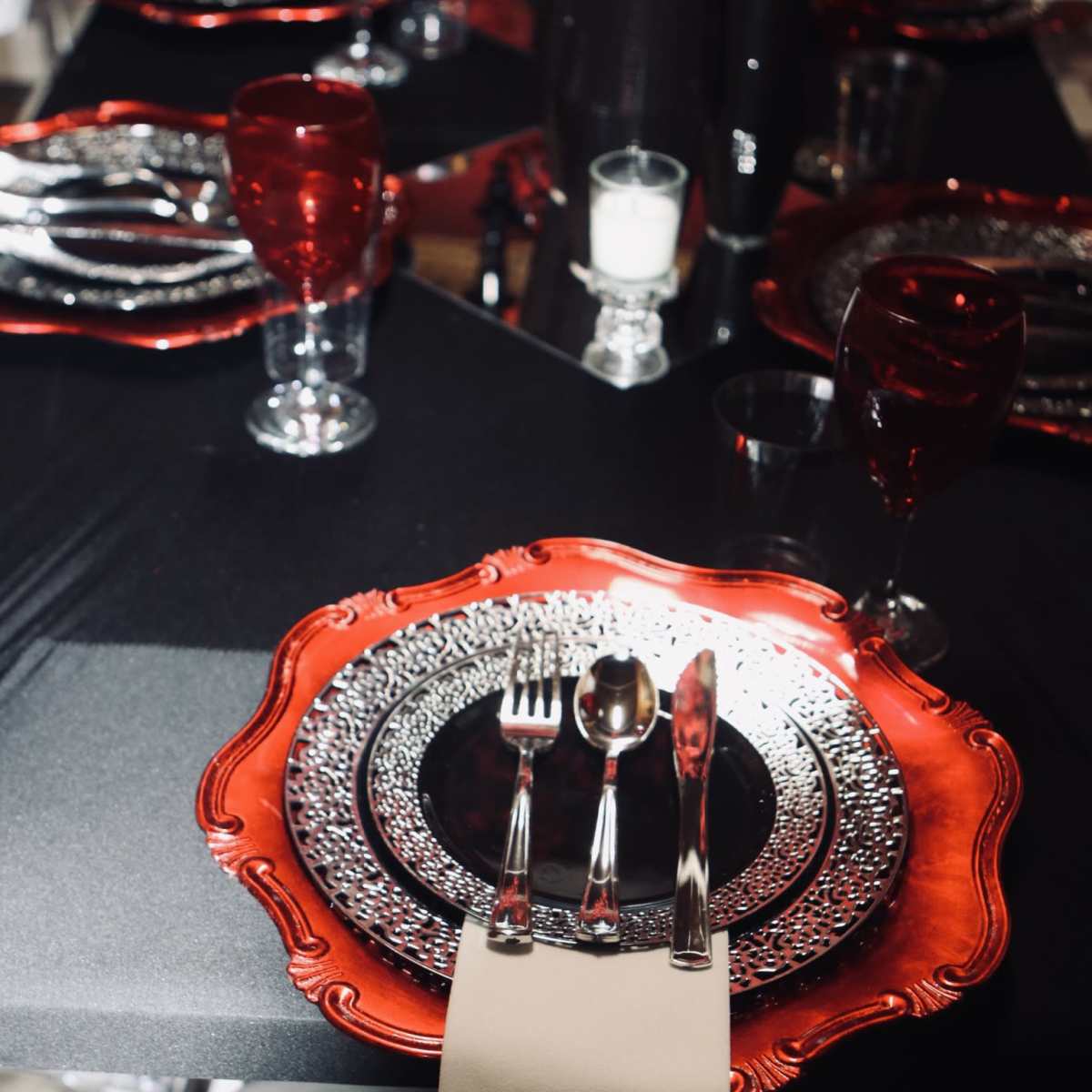 A beautifully arranged dining table set with red and silver plates, sparkling glassware, and neatly placed cutlery on a black tablecloth.