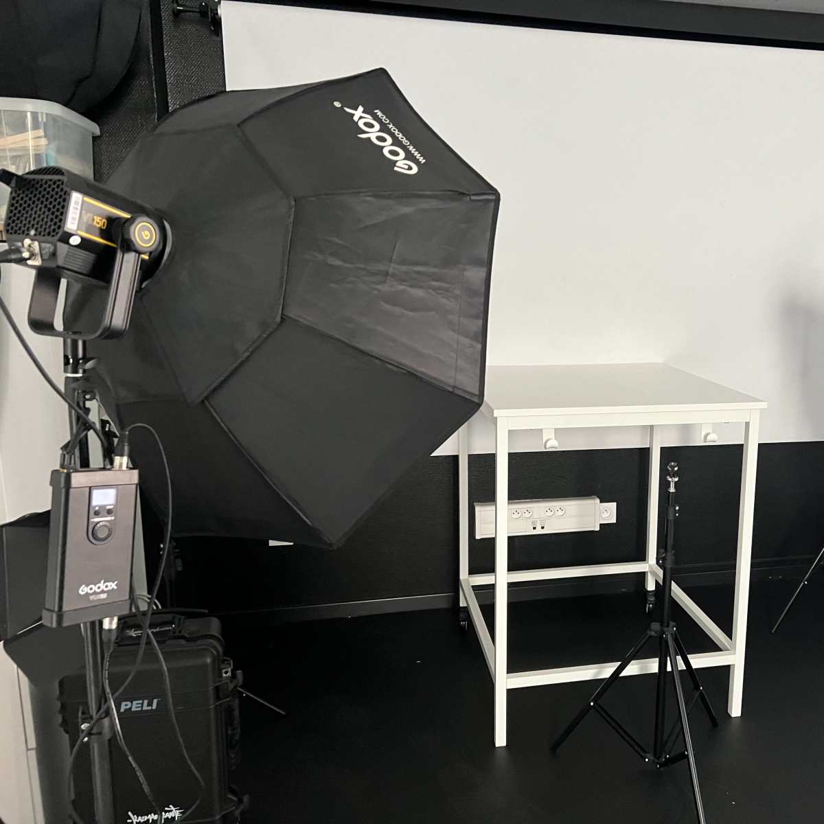 A photography studio setup with two softbox lights, a white backdrop, and a table positioned in the center.