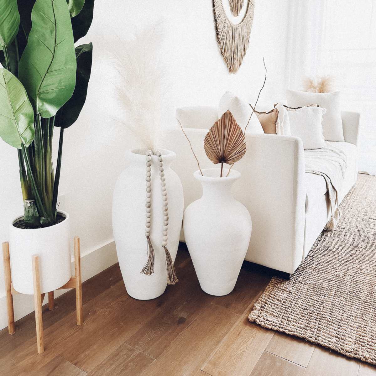 A modern living room with a white sofa, two large white vases, a tall potted plant, and decorative elements on the walls and floor.
