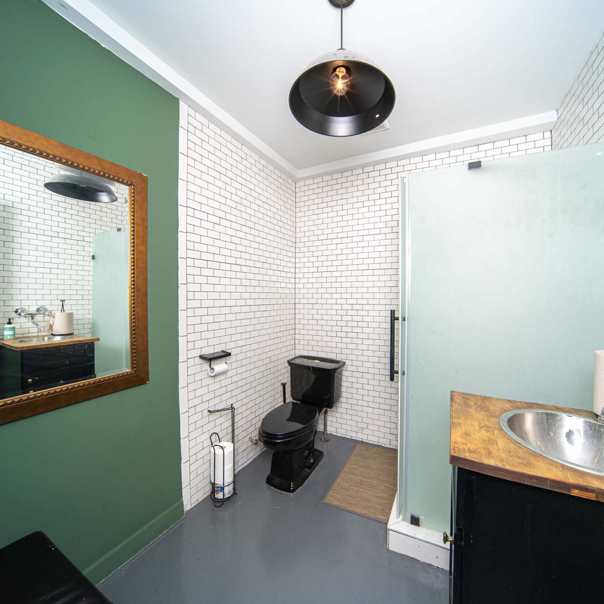 A modern bathroom with white tiled walls, a wooden sink, a black toilet, and a large mirror.