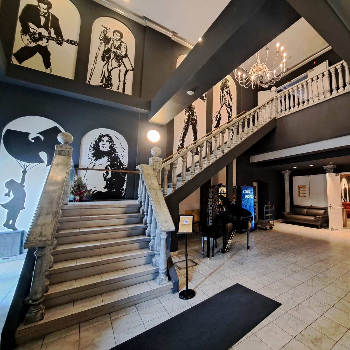 A spacious lobby with a grand staircase, adorned with large black-and-white murals of musicians, and a decorative fountain on the right.