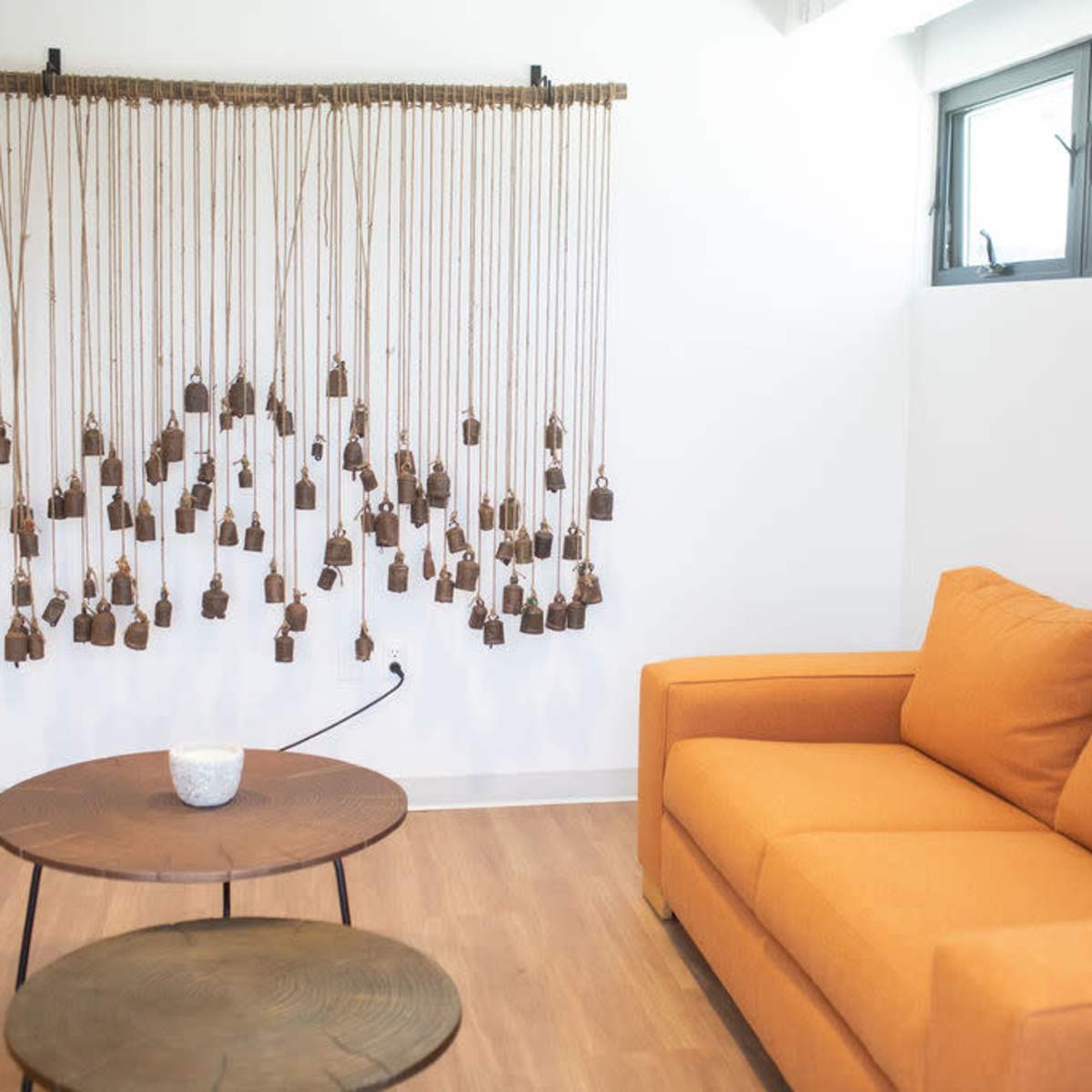 A cozy indoor space features an orange sofa, a wooden coffee table, and a hanging art installation made of small brown bells.