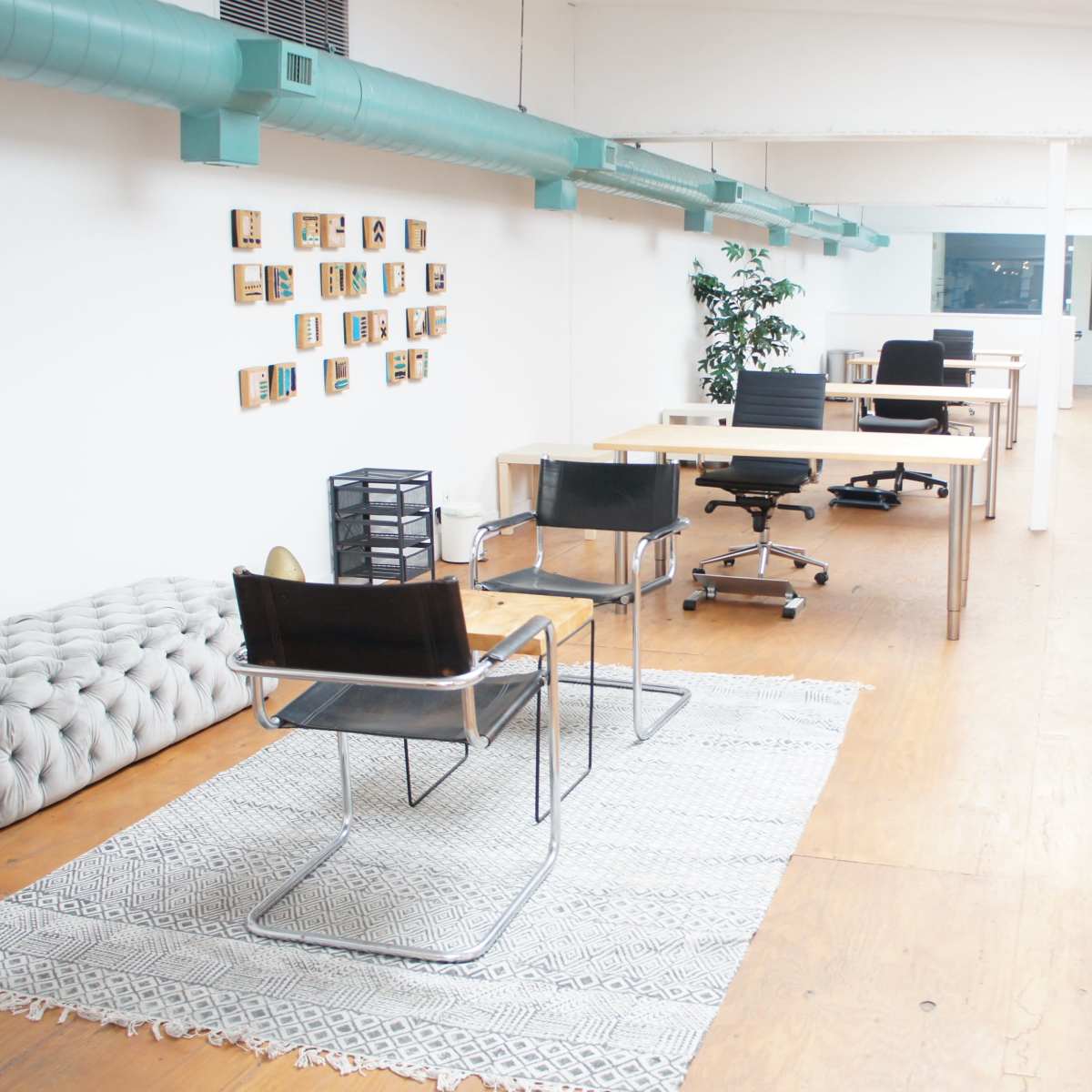 A spacious office layout with several wooden desks, black chairs, a decorative rug, and wall art.