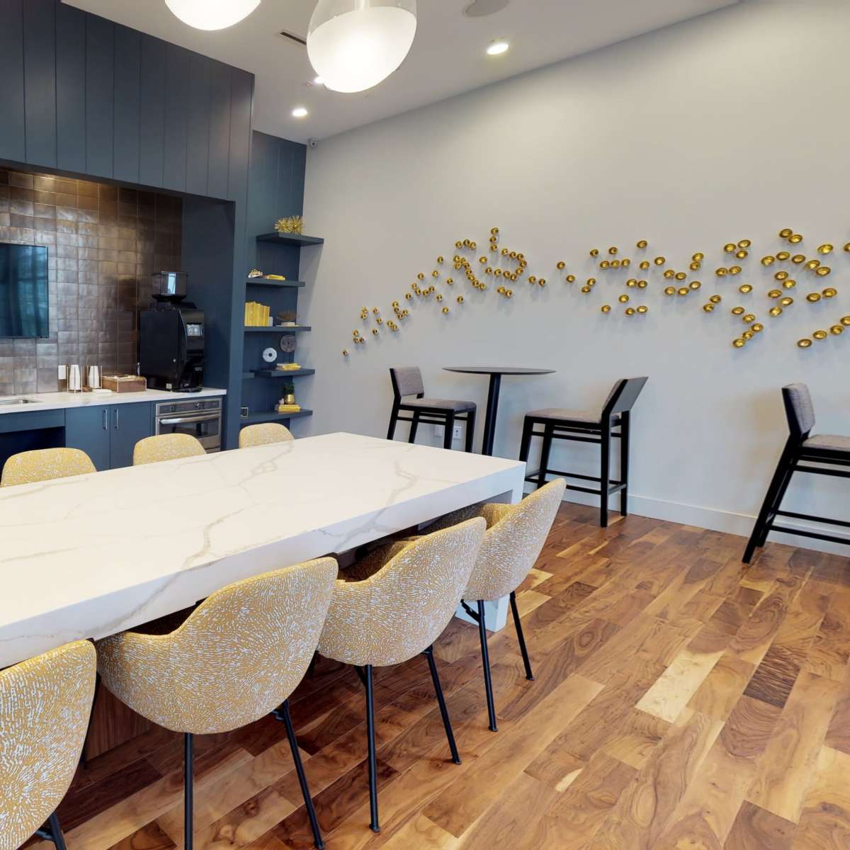 A modern kitchen area with a large marbled table and stylish seating, a backsplash of brown tiles, and a television mounted on the wall.