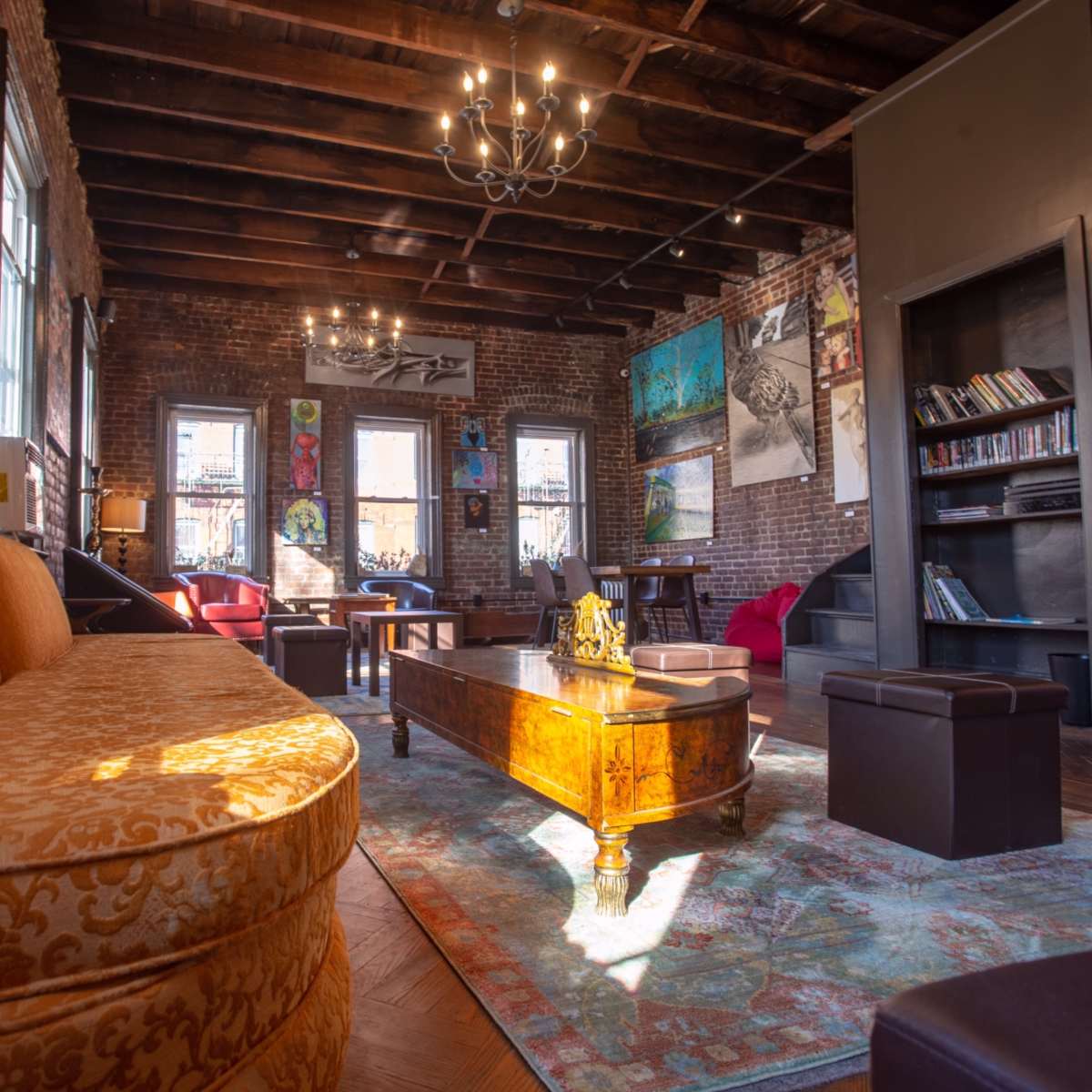 A spacious living room with exposed brick walls, wooden beams, and a mix of seating arrangements, including a large orange couch and coffee tables.