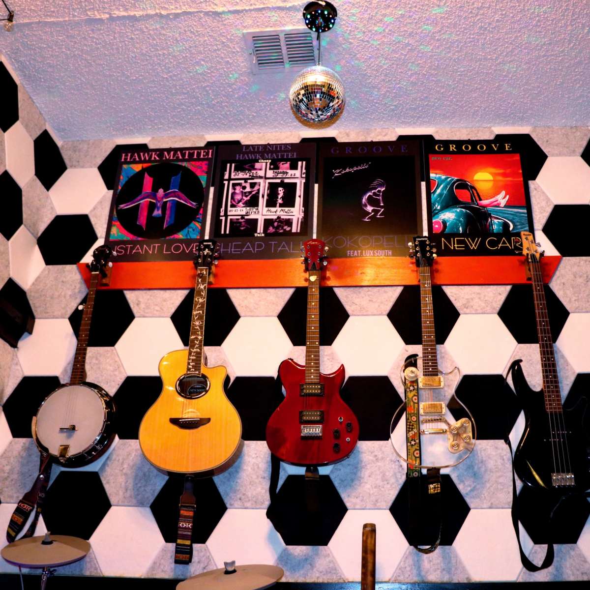A wall adorned with various guitars and drum equipment, alongside framed music posters in a room with a black and white hexagonal pattern.