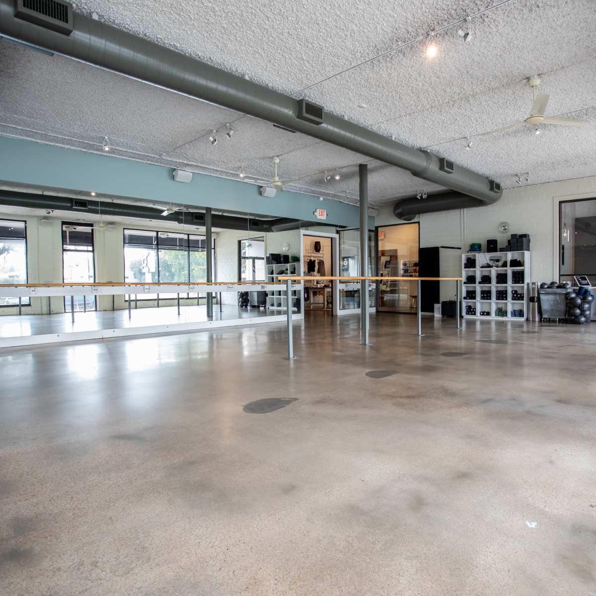 An empty dance studio with a polished concrete floor, large mirrors along one wall, and natural light coming through the windows.
