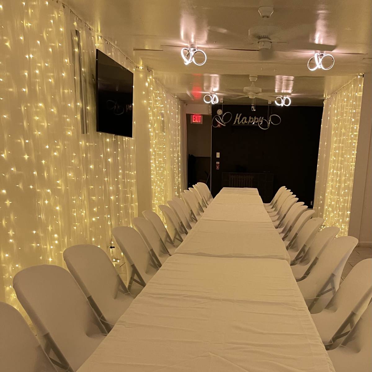 A long, white-covered table is set up in a dimly lit room adorned with twinkling fairy lights along the walls.