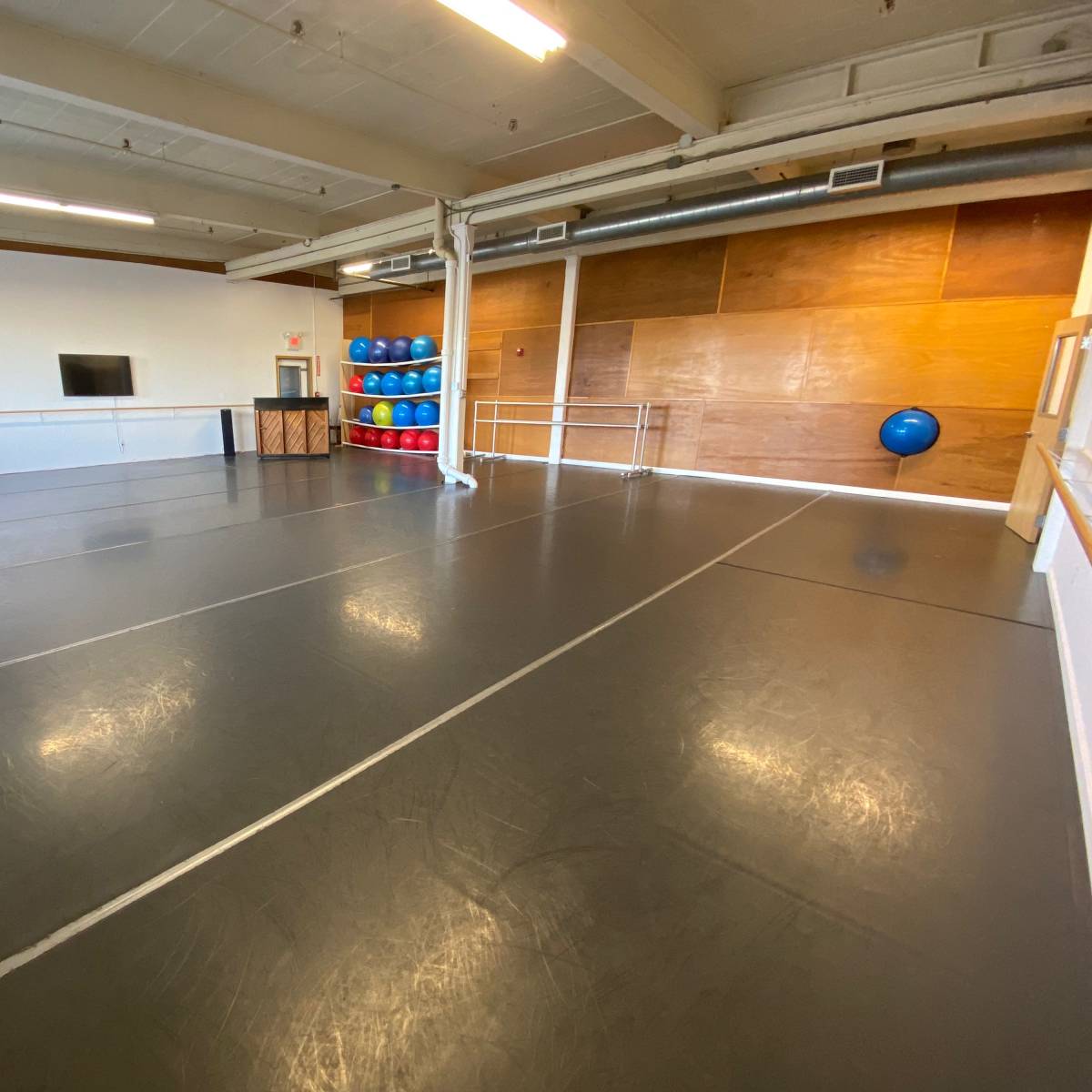 A spacious fitness studio with a smooth gray floor, mirrored walls, and various fitness equipment stacked in the corner.