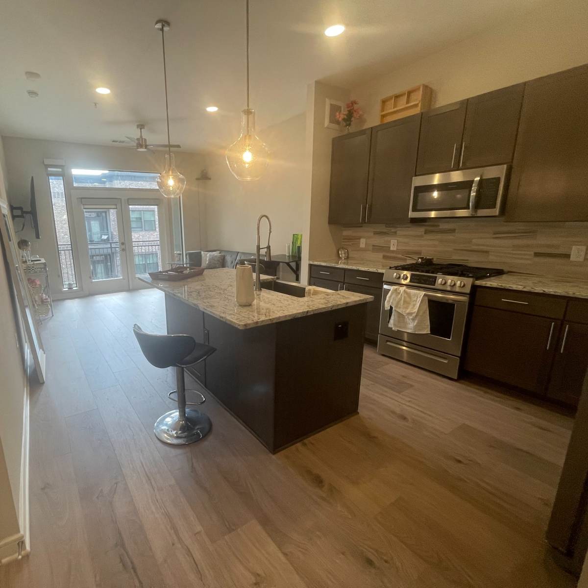 A modern kitchen with granite countertops, dark cabinetry, a stainless steel stove, and a small dining area featuring a bar stool.