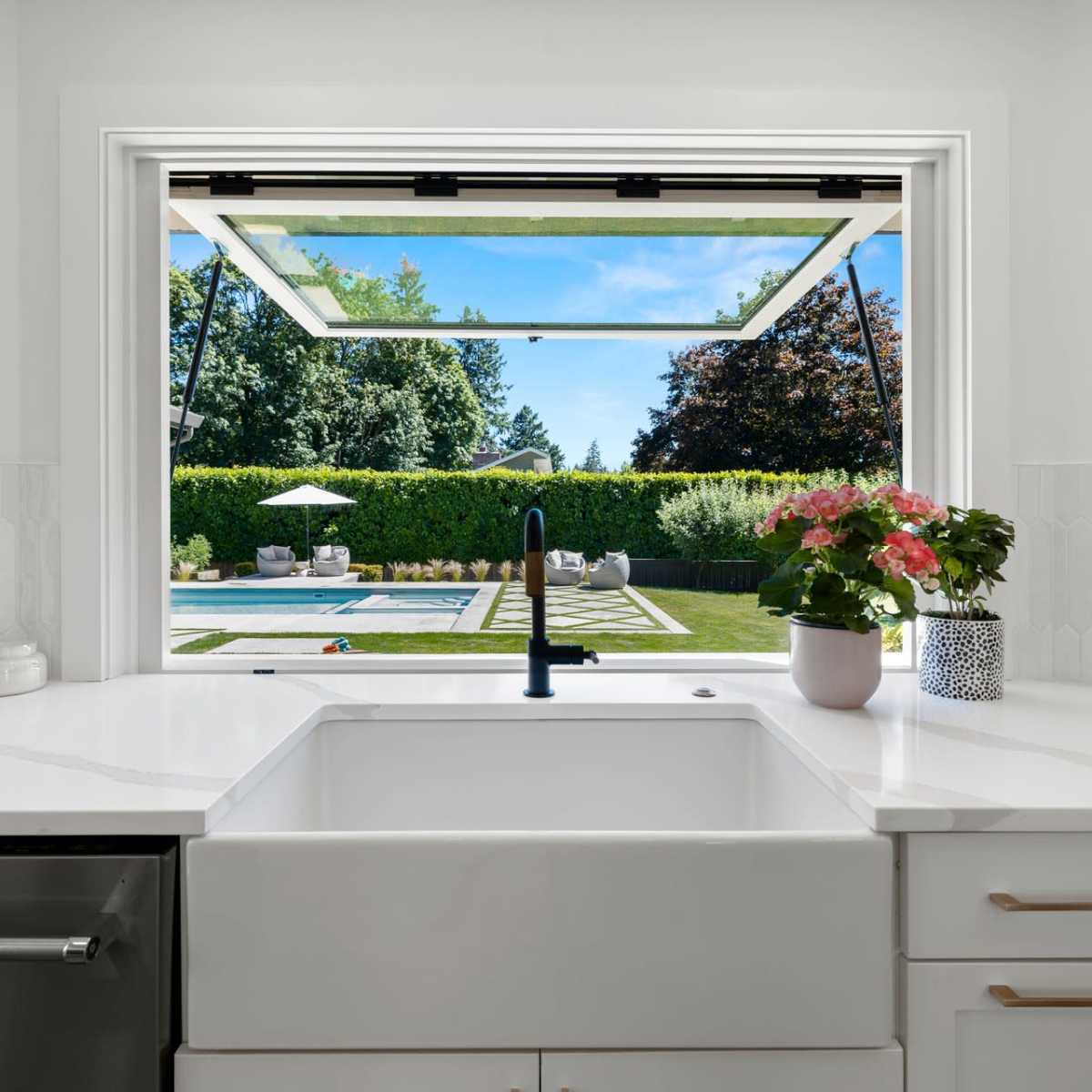 A modern kitchen features a view of a landscaped outdoor pool area through a large open window.