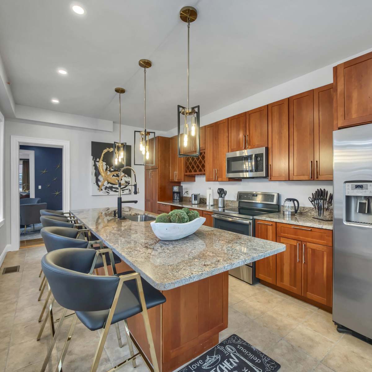 A modern kitchen features dark wood cabinetry, stainless steel appliances, and a central island with bar stools and pendant lighting.