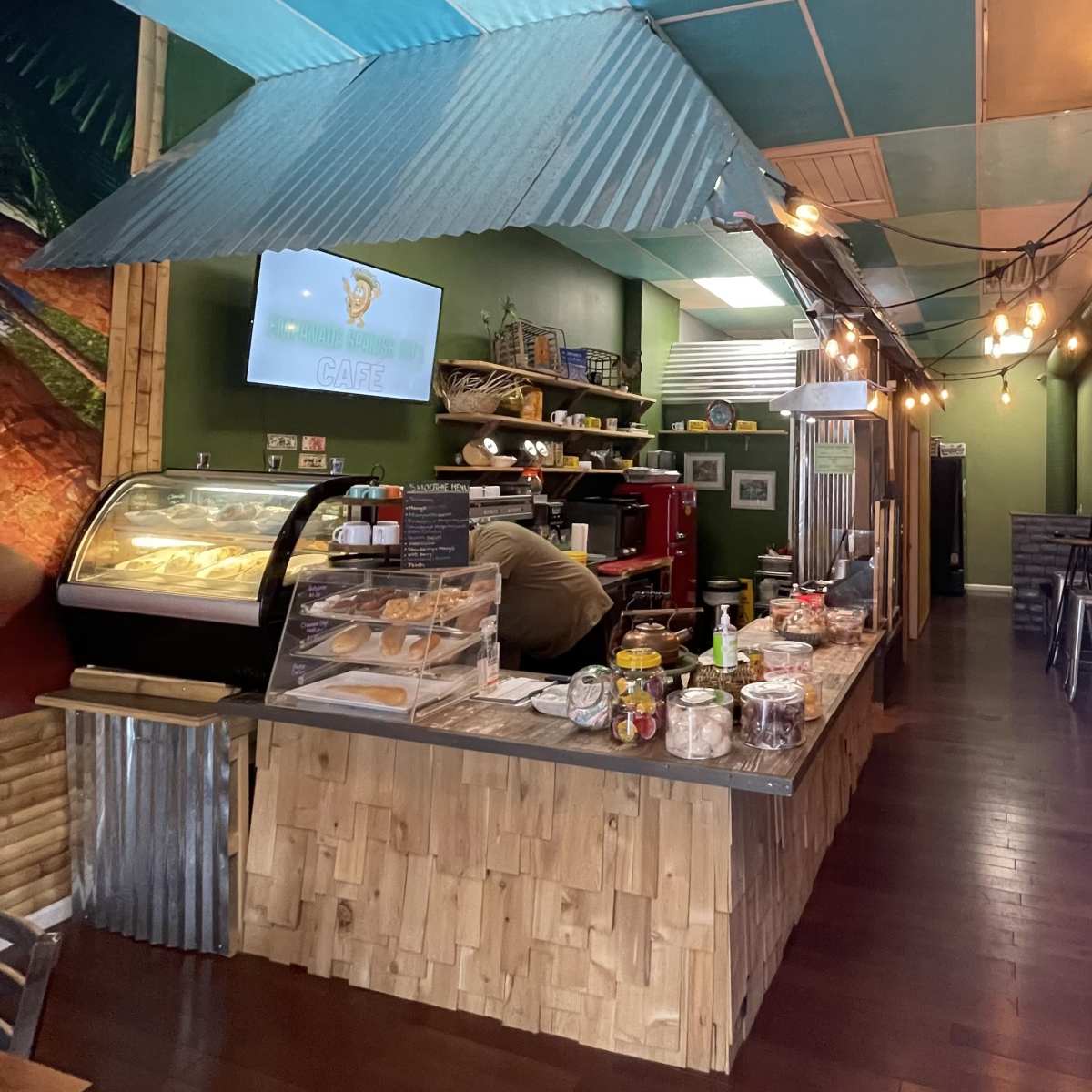 A café interior features a service counter with baked goods and a display case, surrounded by colorful walls and decorative lighting.