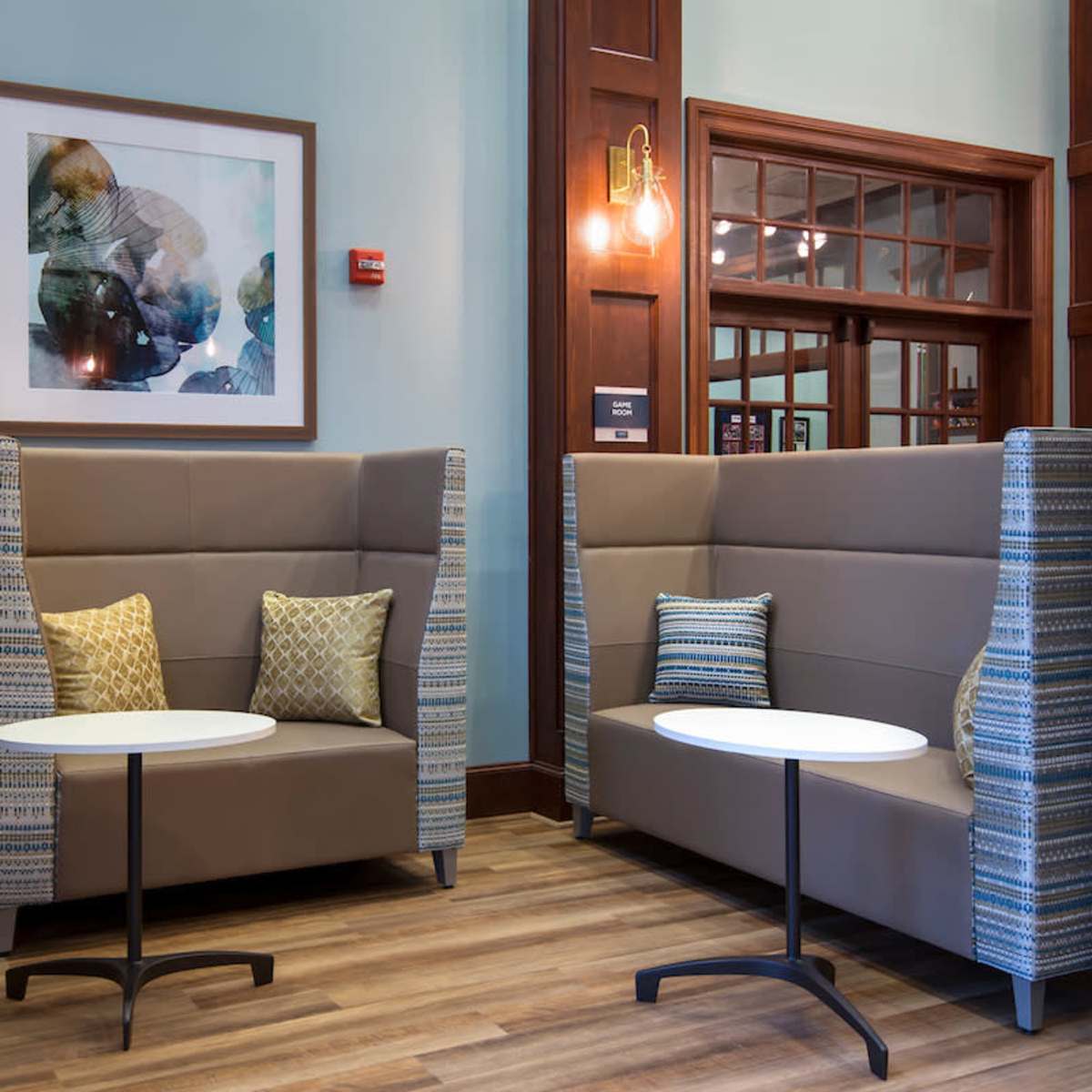 A lounge area with two cozy seating booths and small round tables, framed by wooden walls and a colorful piece of artwork on the wall.