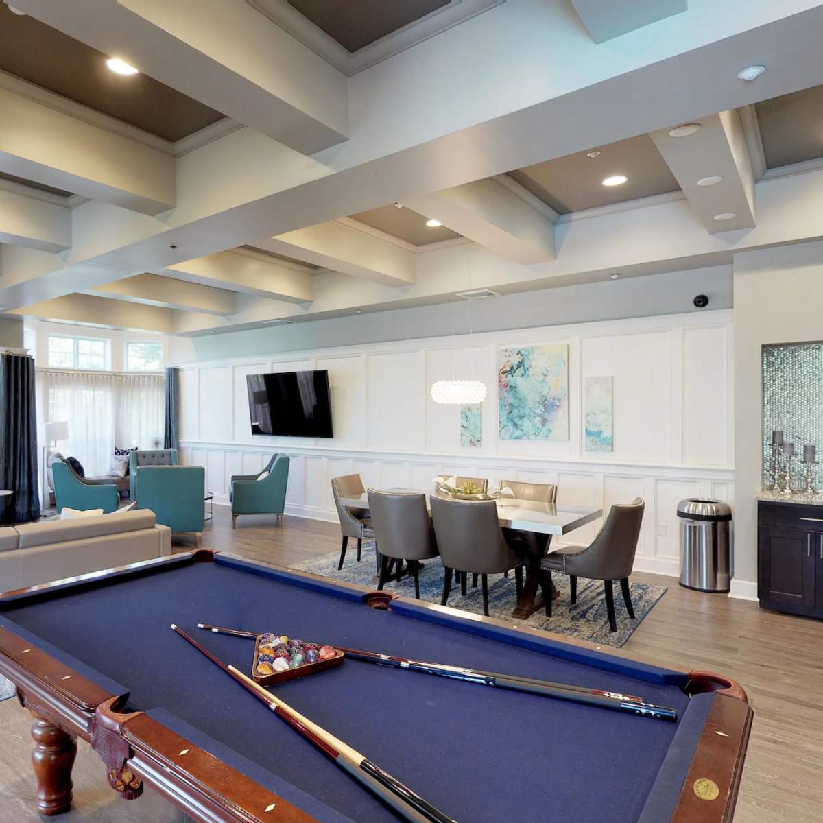 A spacious room features a billiard table in the foreground, a seating area with a fireplace, and a dining area with modern furnishings.