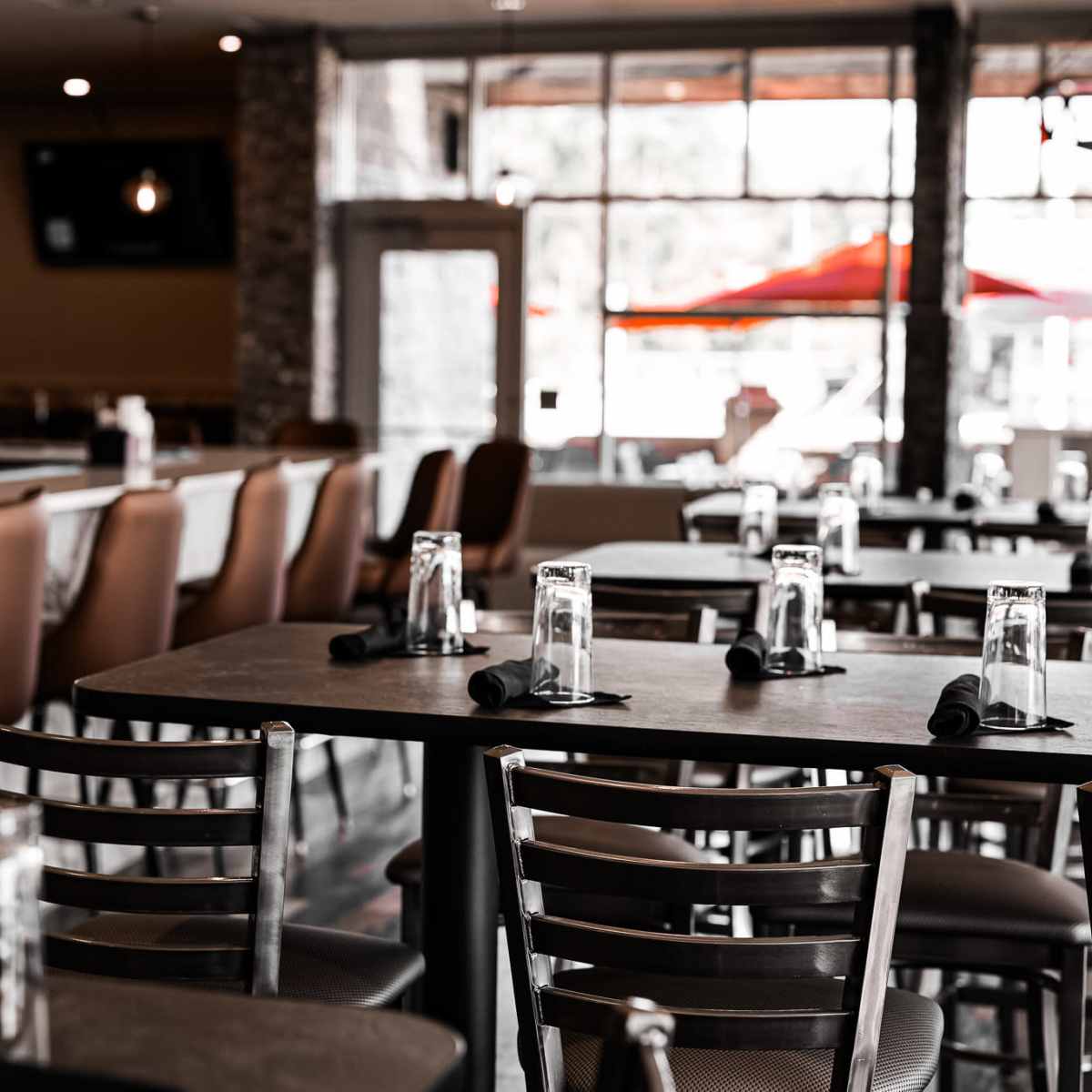 A modern restaurant interior with empty tables and chairs, and a bar area in the background.