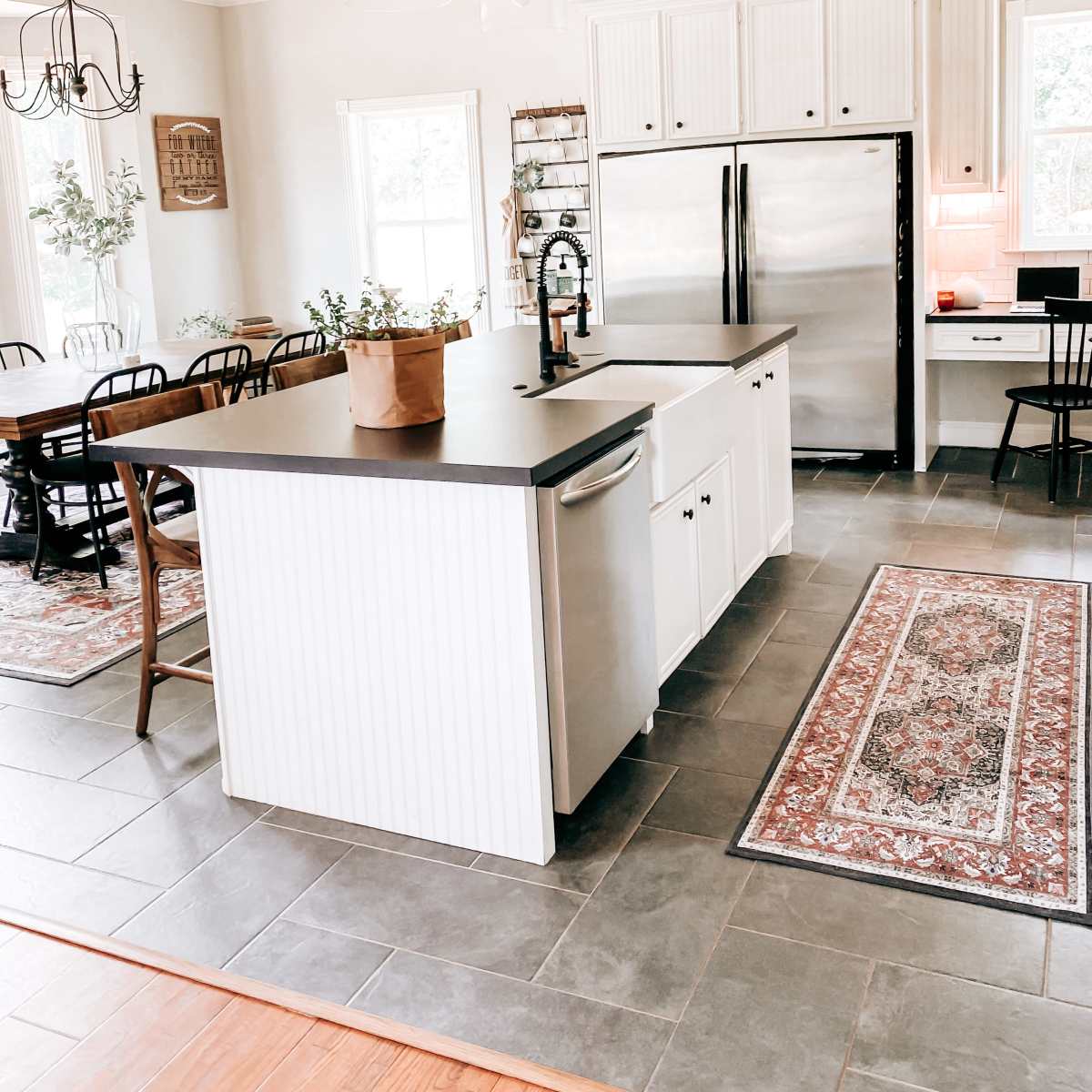 A modern kitchen features a central island with a dark countertop, white cabinetry, stainless steel appliances, and a combination of dining and prep areas.