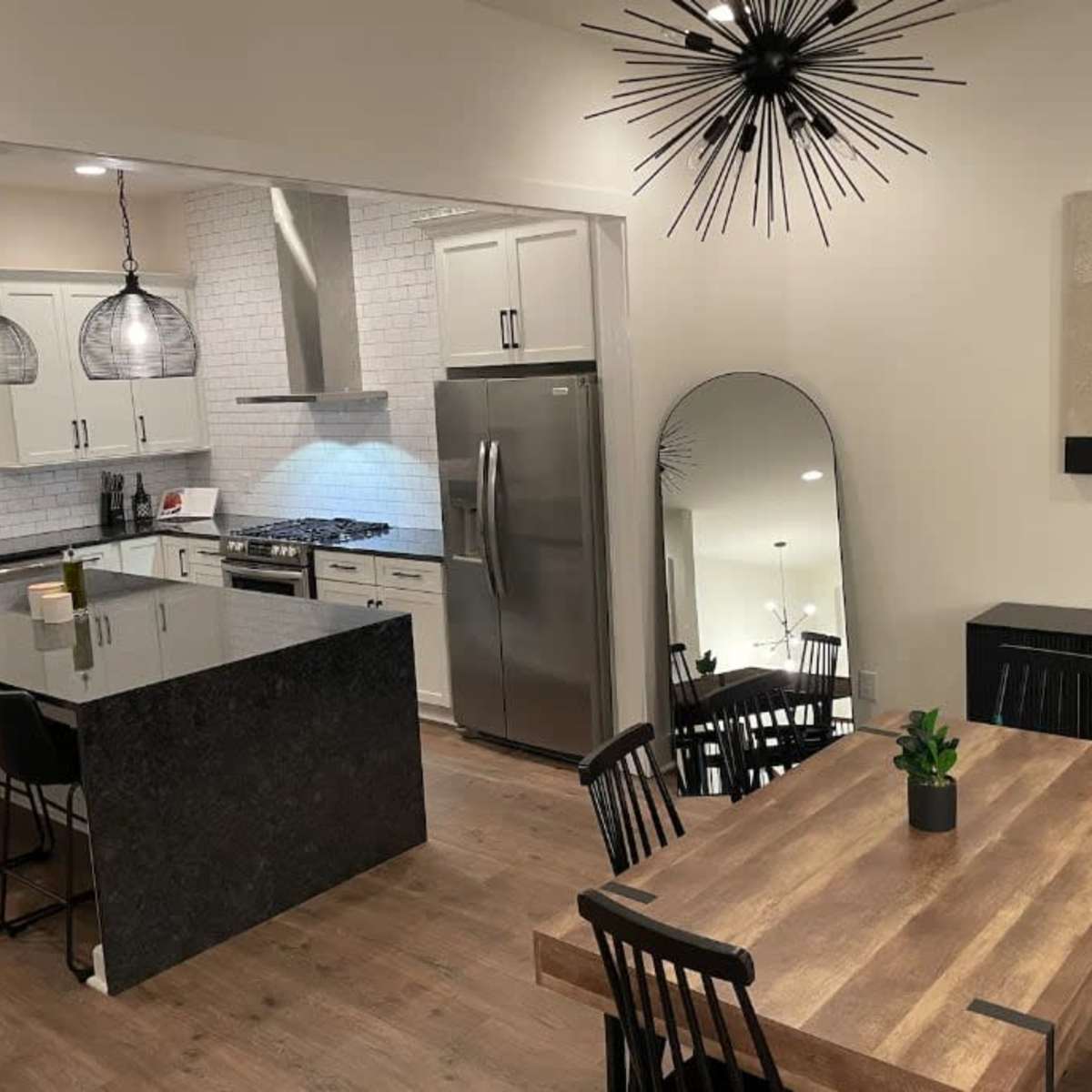 A modern kitchen and dining area featuring a large island with barstools, a sleek dining table, and a decorative mirror.