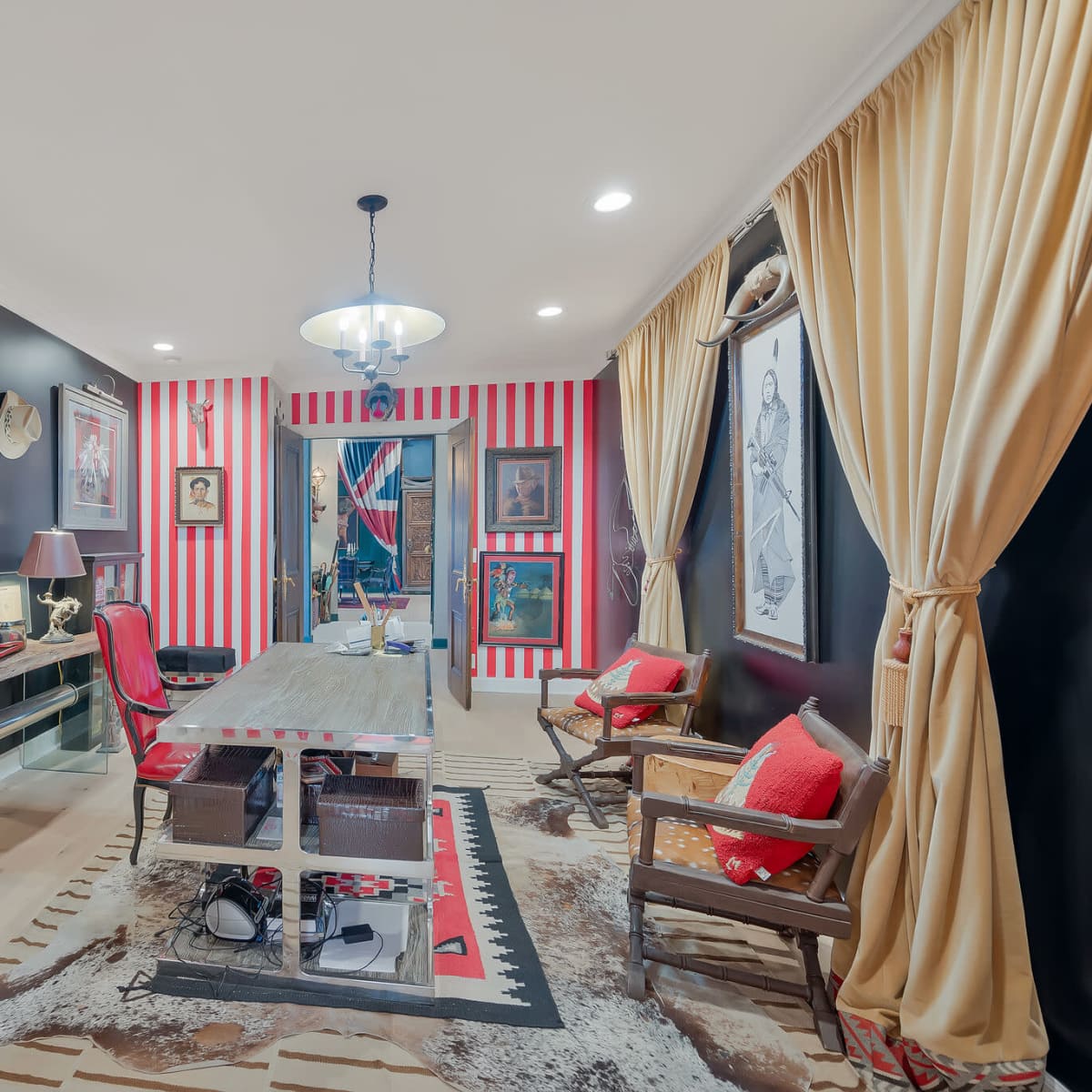 A home office featuring black and red striped walls, wooden furniture, framed artwork, and vintage hats displayed on the wall.