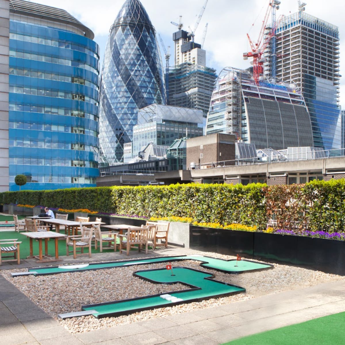 A rooftop mini-golf course surrounded by high-rise buildings in a modern cityscape.