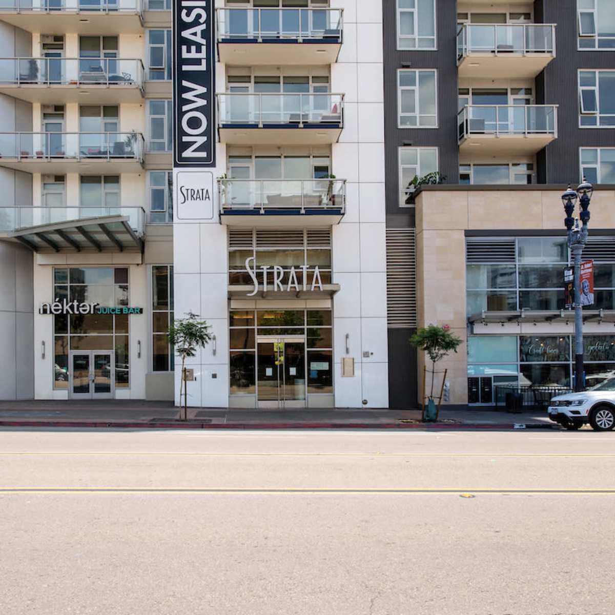A modern multi-story building with a large "Now Leasing" sign and an entrance labeled "Strata," located on a busy street.
