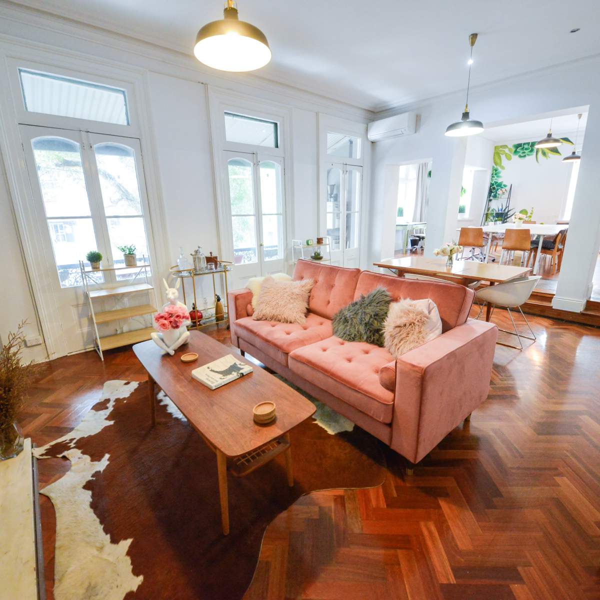A modern living room with a pink sofa, wooden coffee table, and large windows that allow natural light to enter.