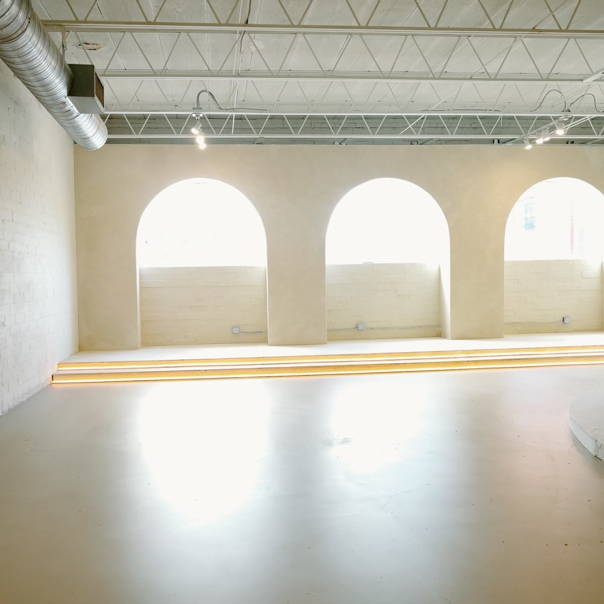 A spacious, minimalist interior with arched windows allowing natural light to illuminate the pale walls and floor.