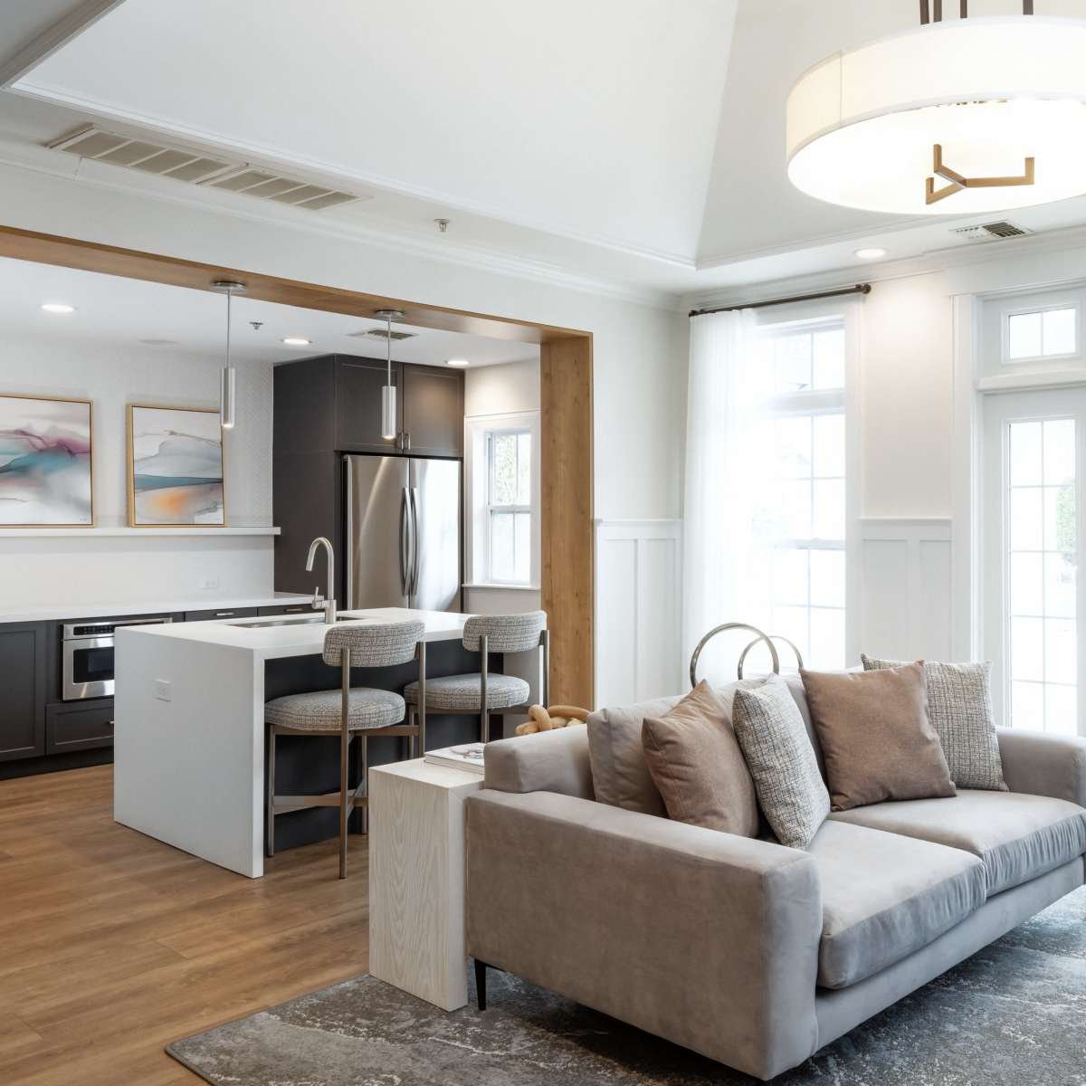A modern living room with a gray sofa, a small round table, and an adjoining kitchen area featuring a sleek design and stainless steel appliances.