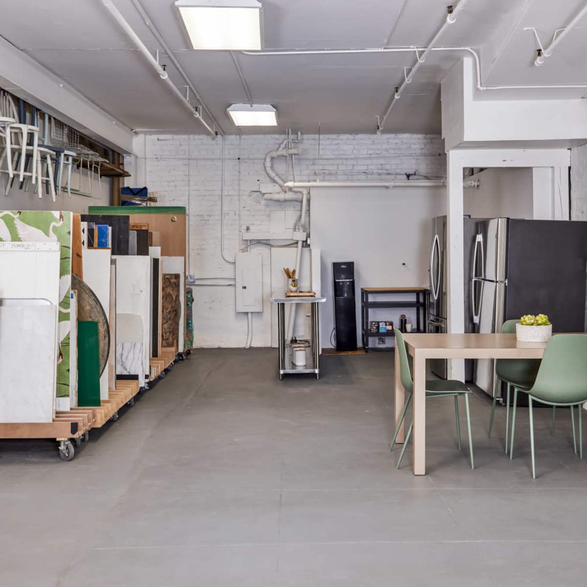 A spacious room features several refrigerators on carts along one side, a table with chairs in the center, and a partitioned area with a curtain.