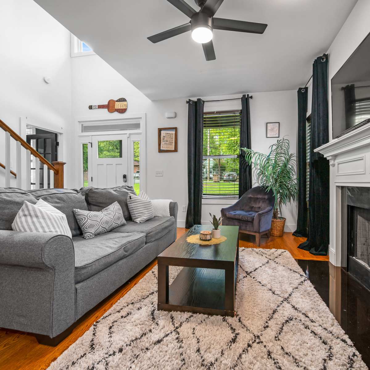 A modern living room features a gray sofa, a coffee table, and a fireplace, with large windows providing natural light.