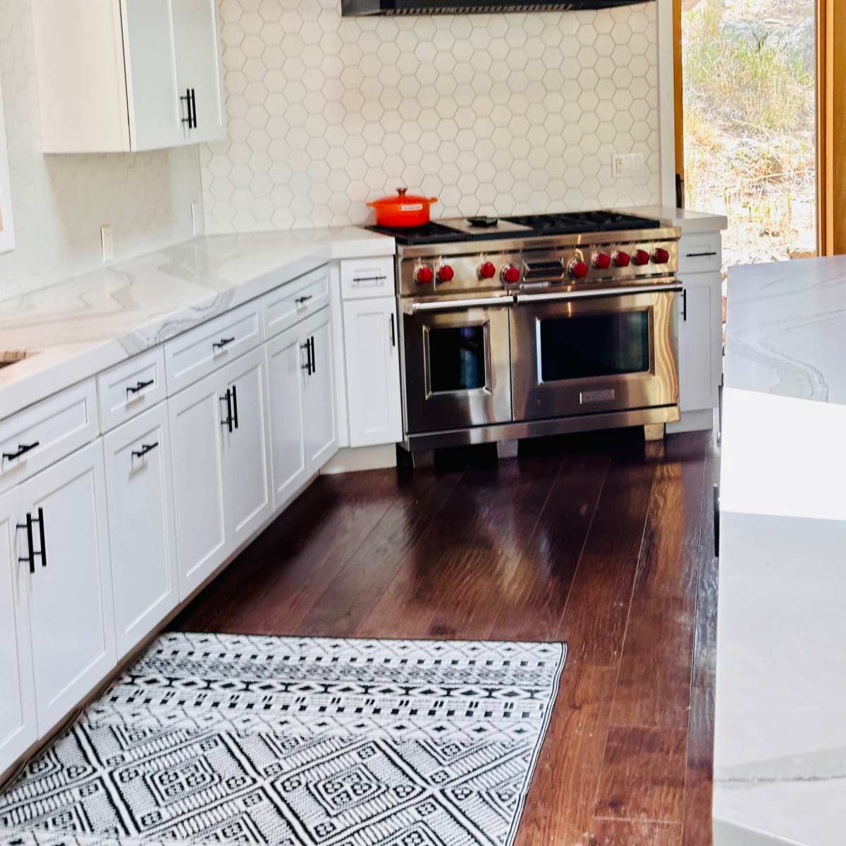 A modern kitchen features white cabinetry, a stainless steel gas range, and a large window with natural light.