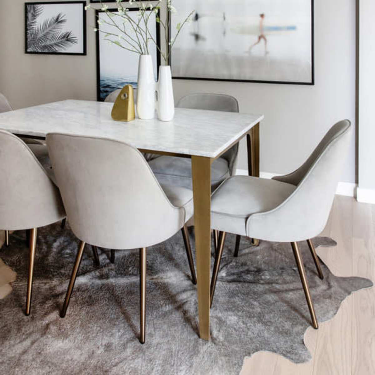 A dining area features a marble-top table surrounded by gray upholstered chairs and decorated with artwork on the walls.