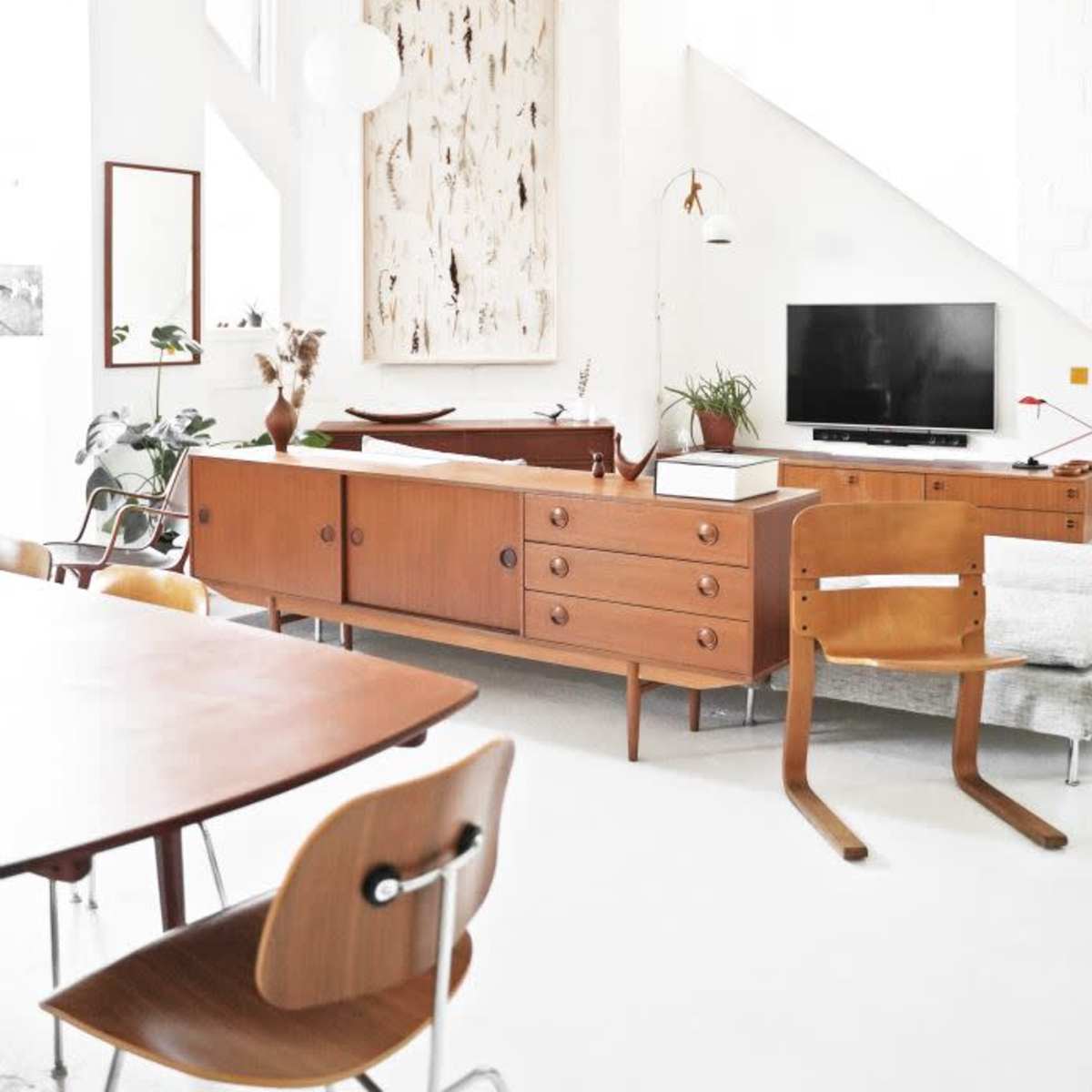 A modern living space with wooden furniture, a TV, and decorative wall art in a light-filled room.