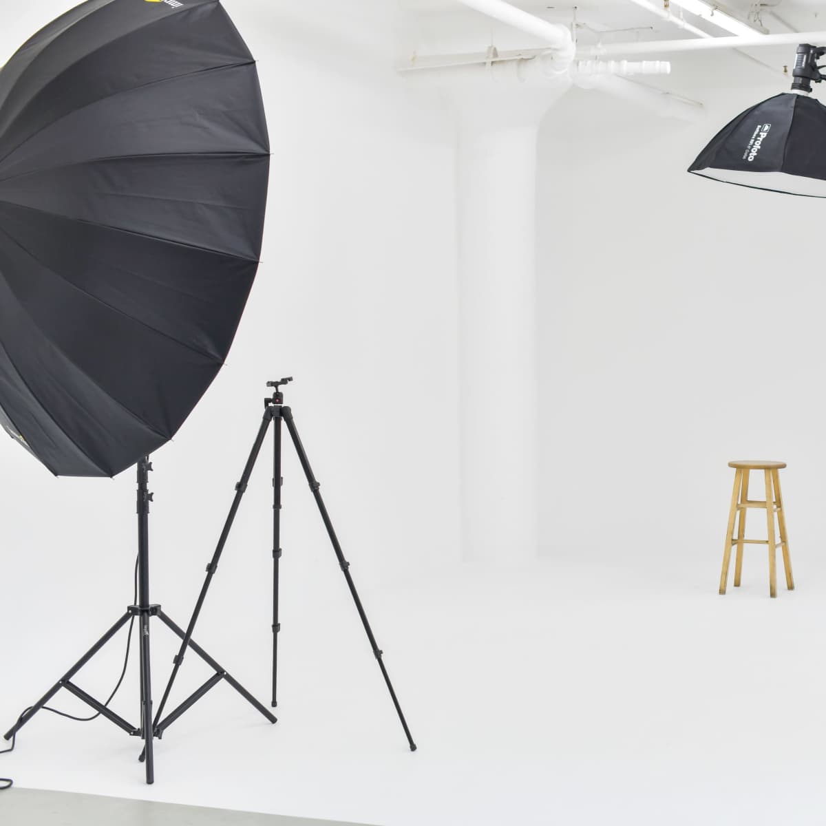A photography studio with a wooden stool, large softbox lights, and light stands set against a plain white background.