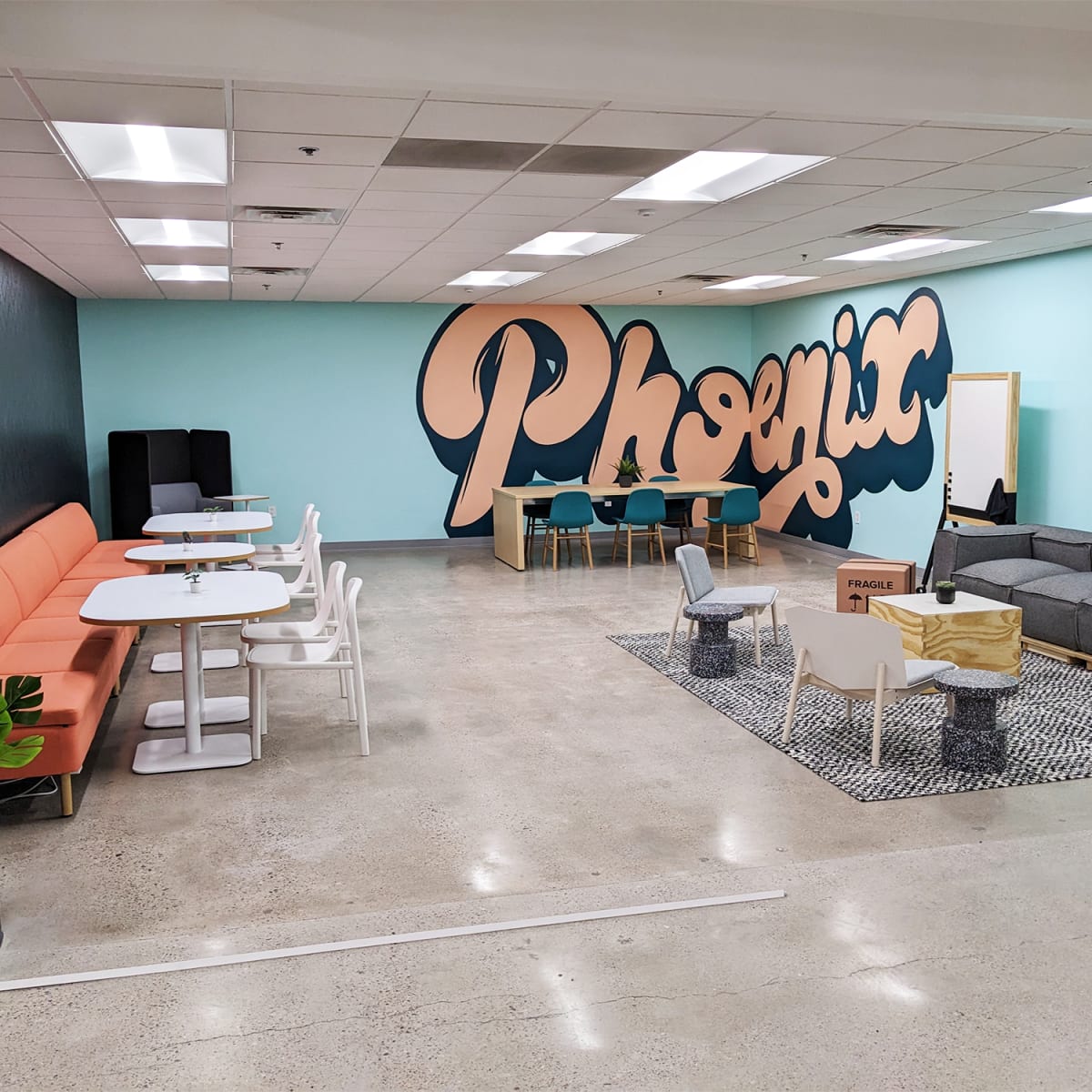 A modern lounge area with colorful seating, tables, and a large mural featuring the word "Phoenix" on the wall.