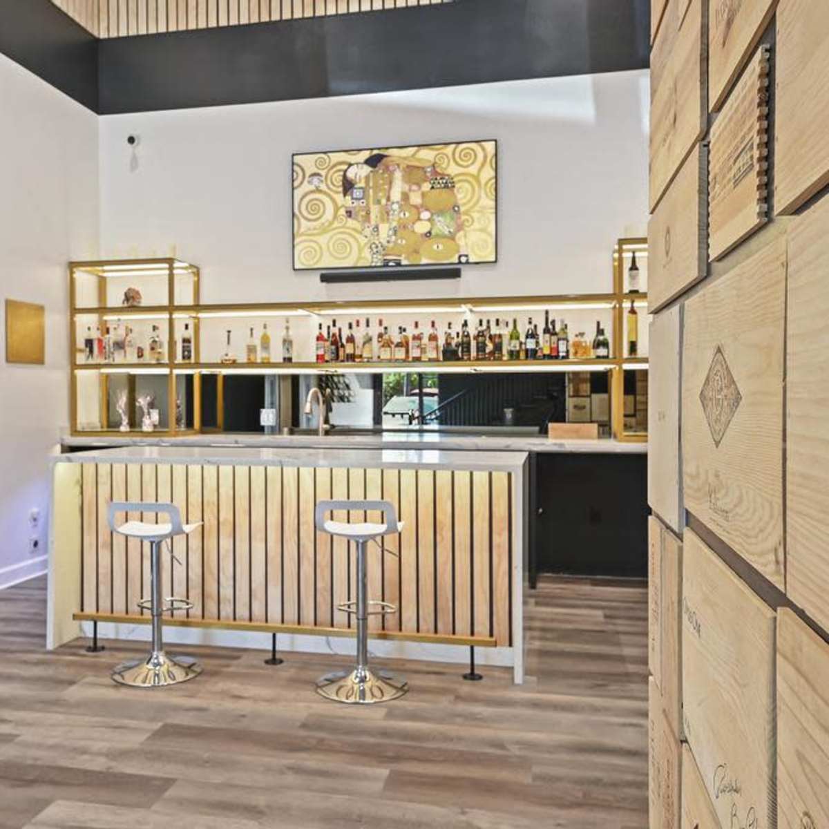 A modern bar area featuring a sleek counter with two stools, a display of various liquor bottles, and a mounted television above.