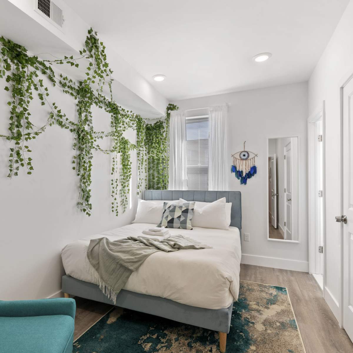 A compact bedroom with a bed, turquoise chair, and decorative greenery on the white walls.