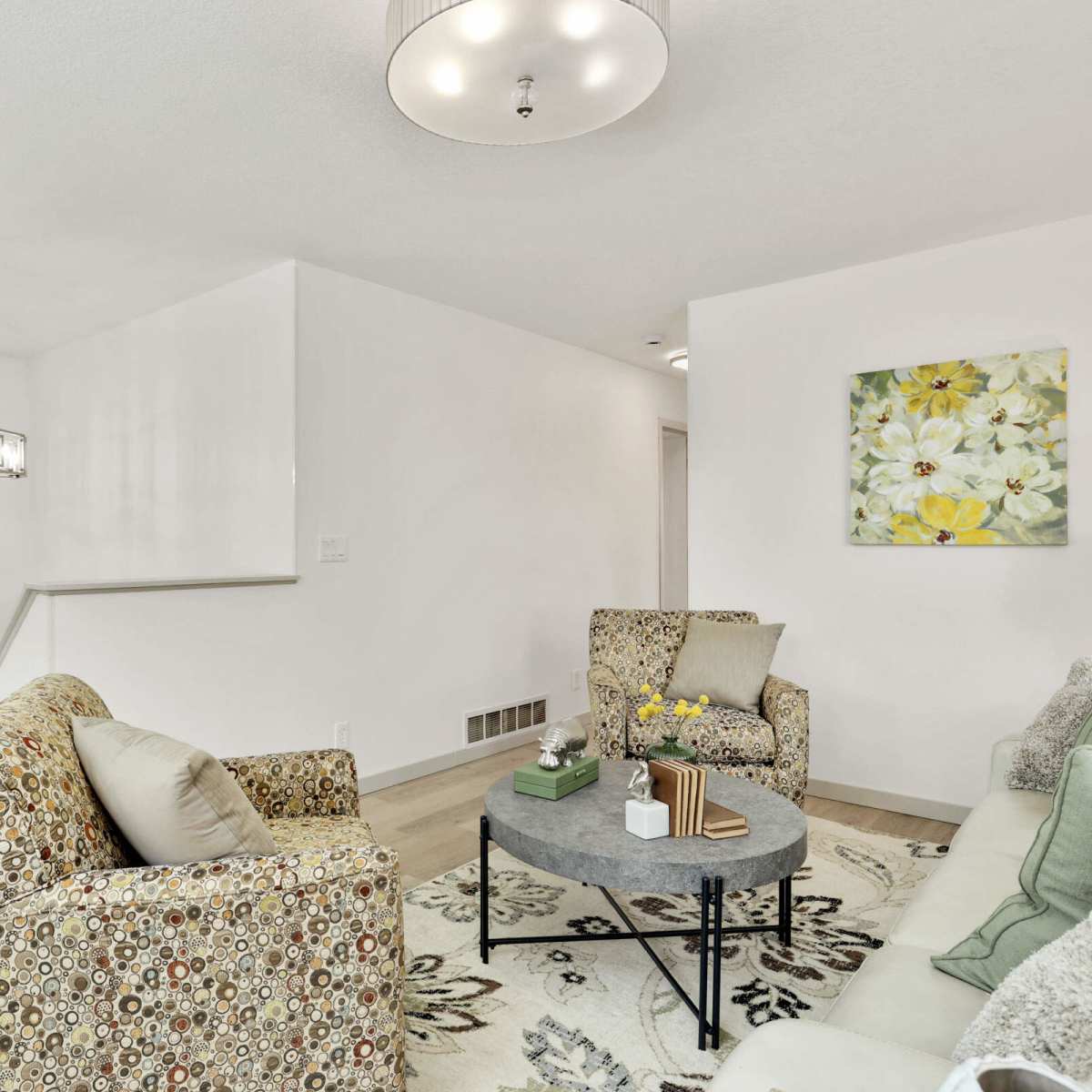A modern living room with two patterned chairs, a round coffee table, and a large floral painting on the wall.