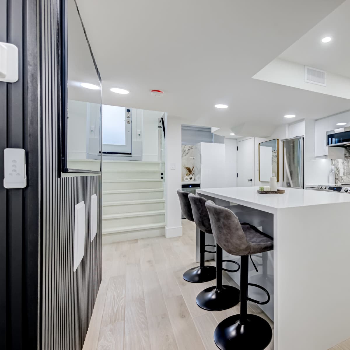 A modern kitchen with a white island, black bar stools, and marble accents on the walls and countertops.