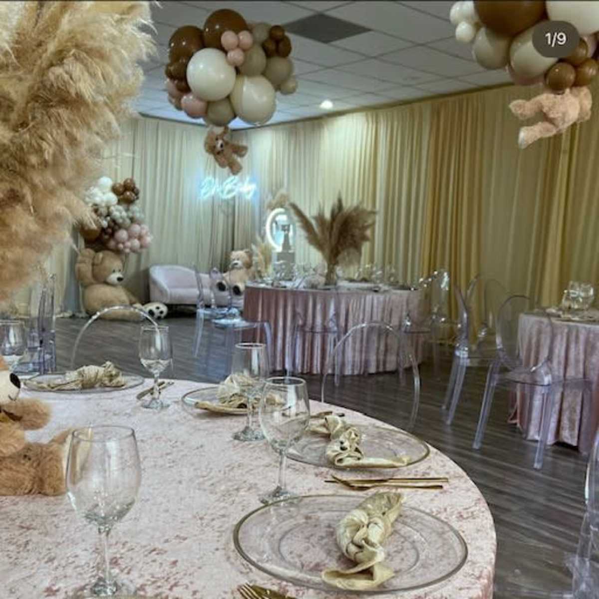 A decorated event space featuring a round table set with glassware and utensils, surrounded by balloons and plush animal decorations.