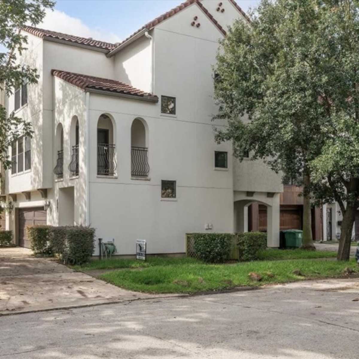 A three-story, Mediterranean-style building with arched balconies, located in a residential area with parked cars and greenery.