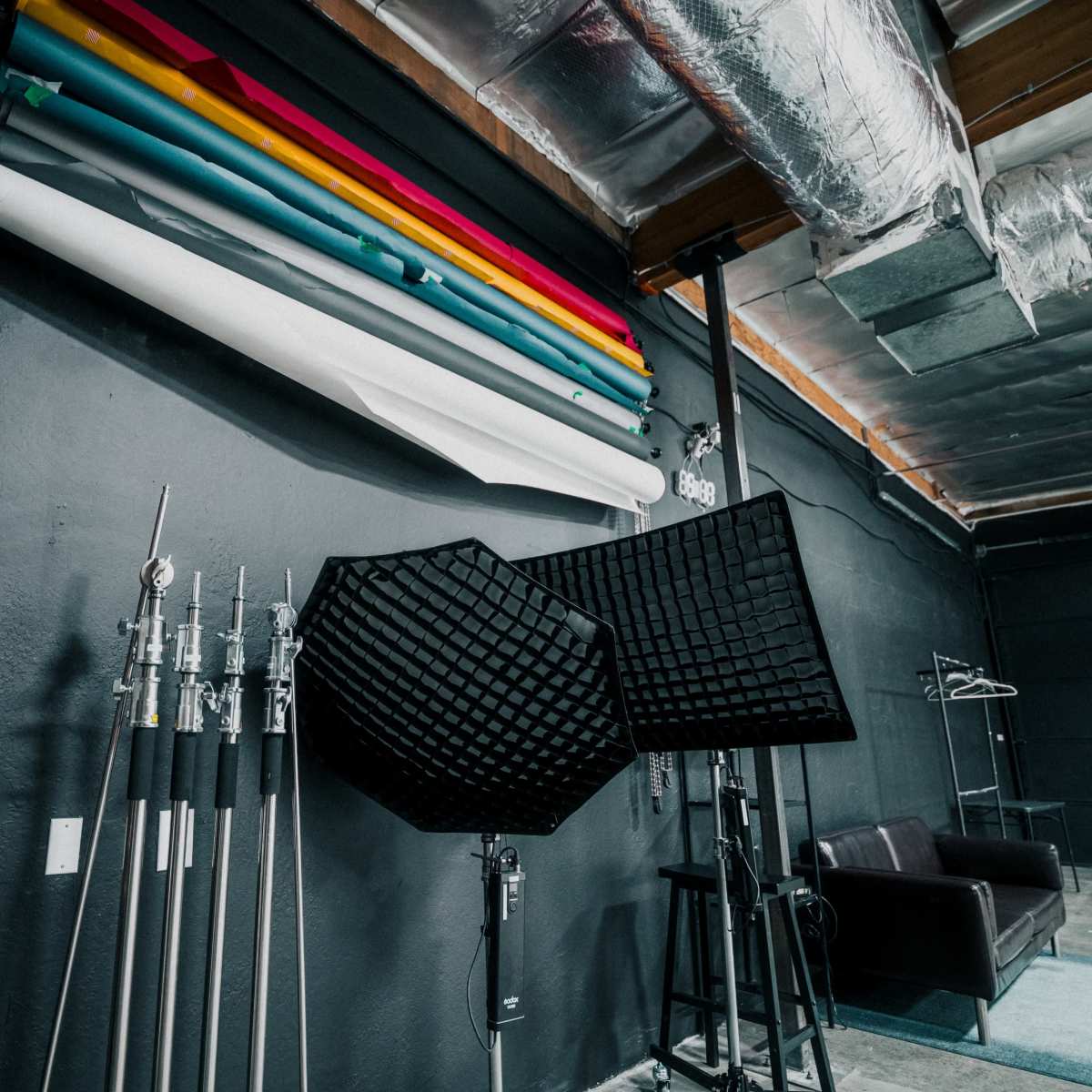 A photography studio with rolled-backdrops, lighting equipment, and a black couch against a dark wall.