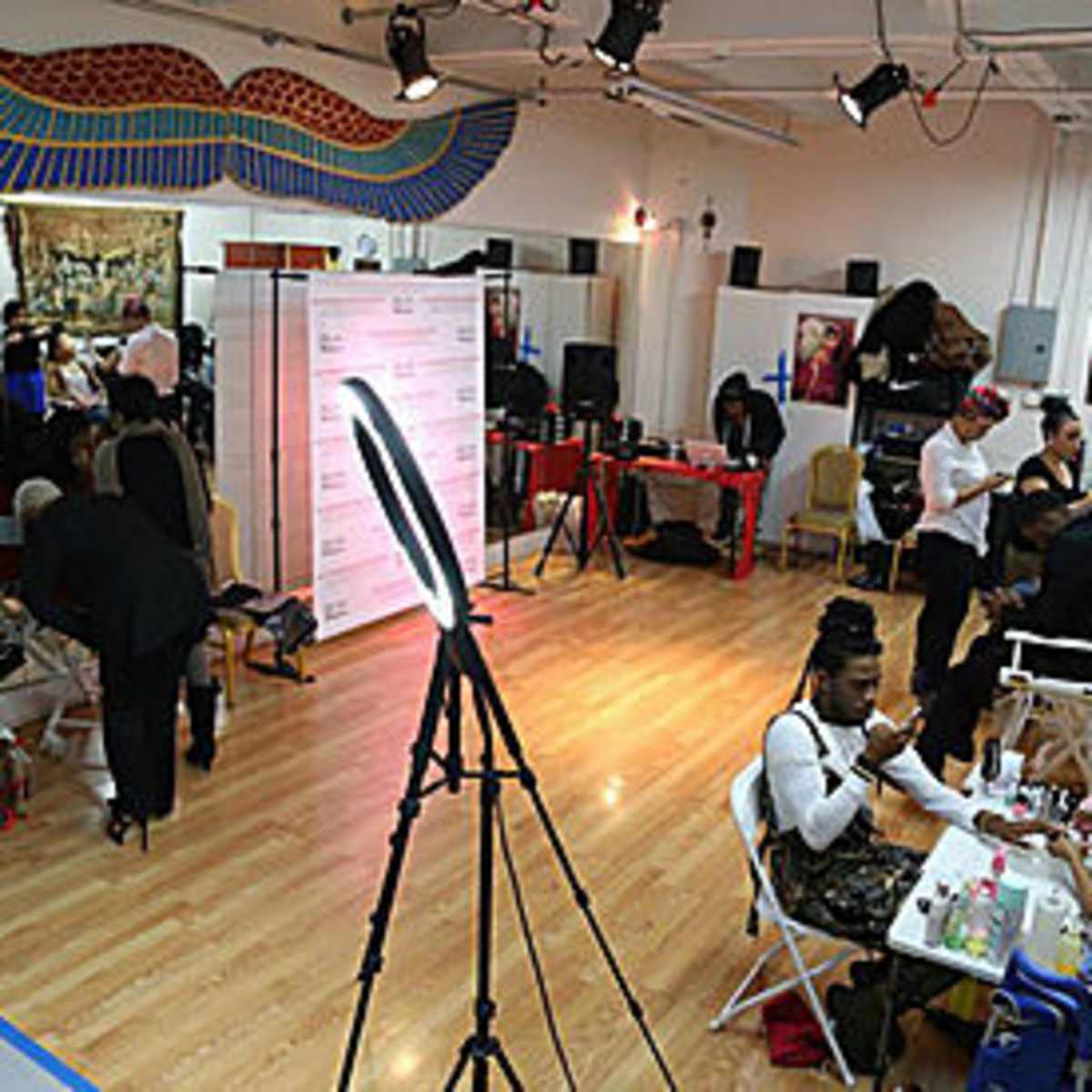 A bustling makeup studio with multiple stations where individuals are receiving beauty treatments and professionals are working on various clients.